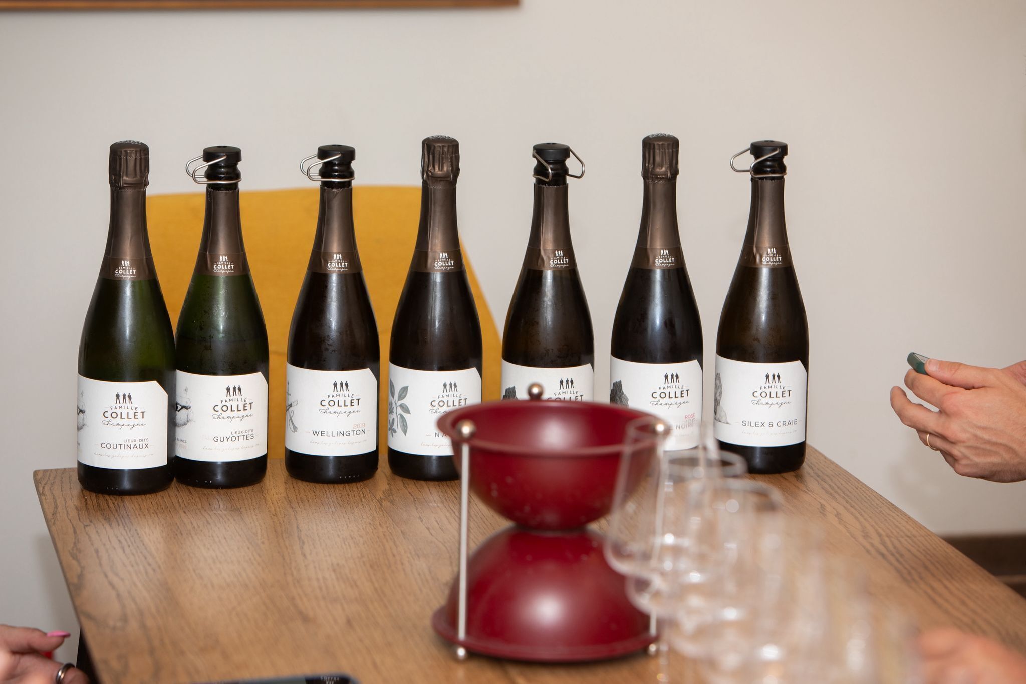 A wooden table with six wine bottles labeled 'Famille Collet' and a red hourglass.