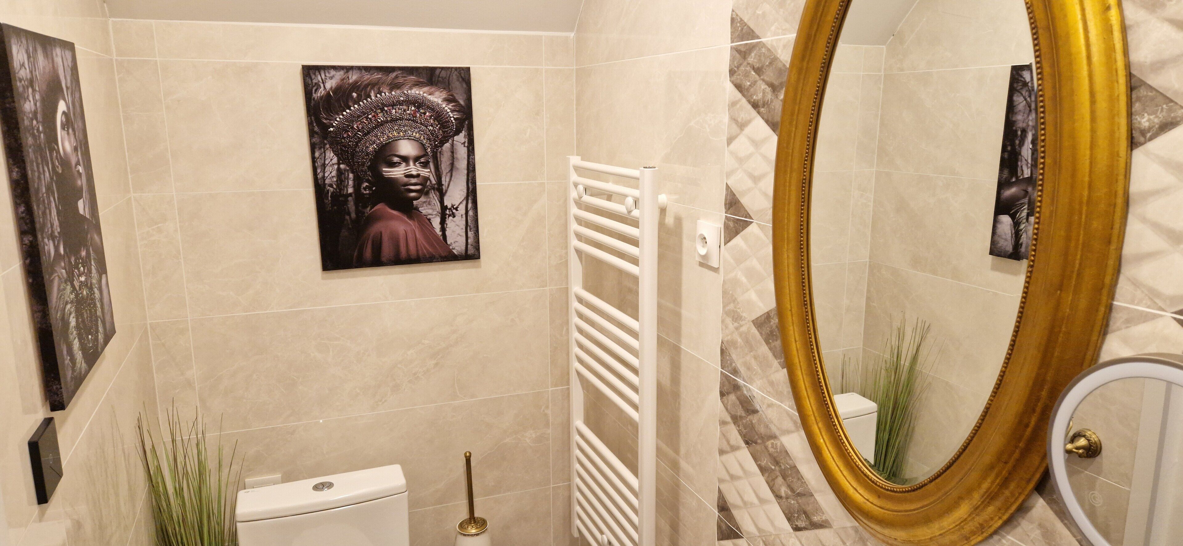 A bathroom with a toilet, a towel rack, a mirror with a gold frame, and artwork on the walls.