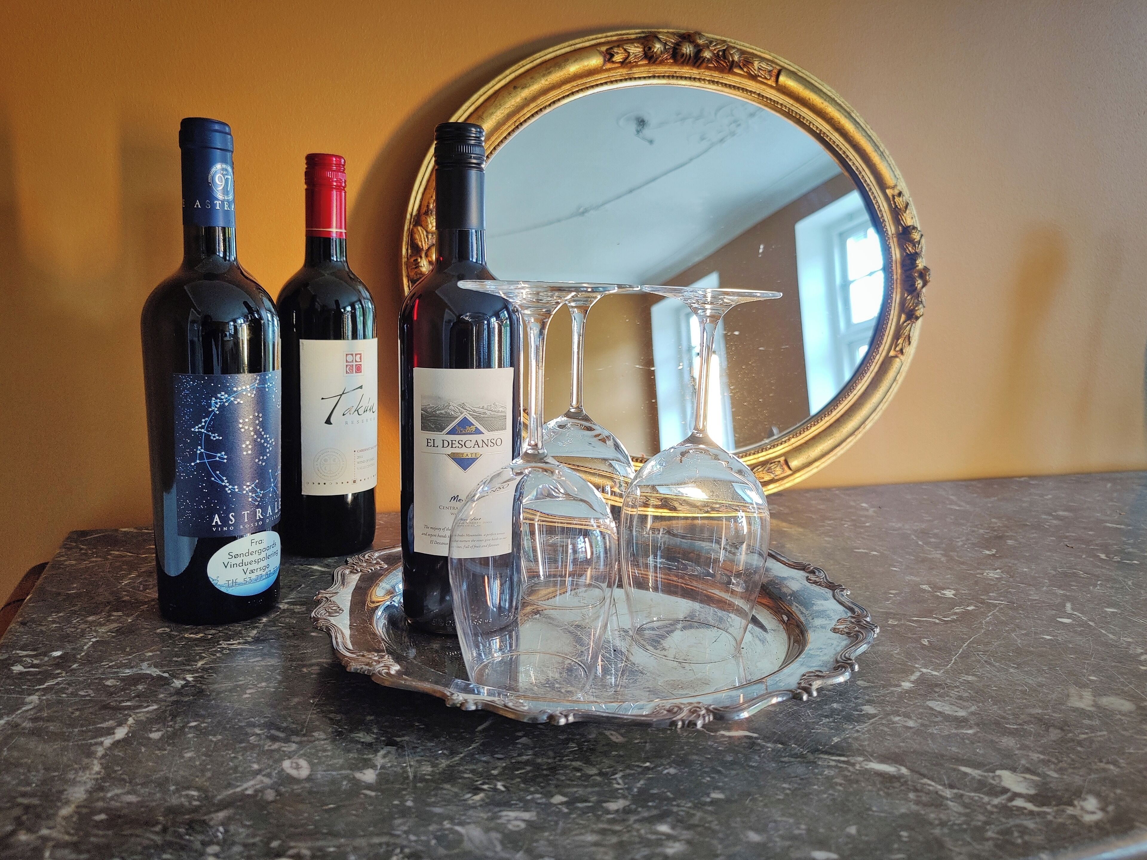 Three wine bottles and two wine glasses on a marble table with a decorative tray.