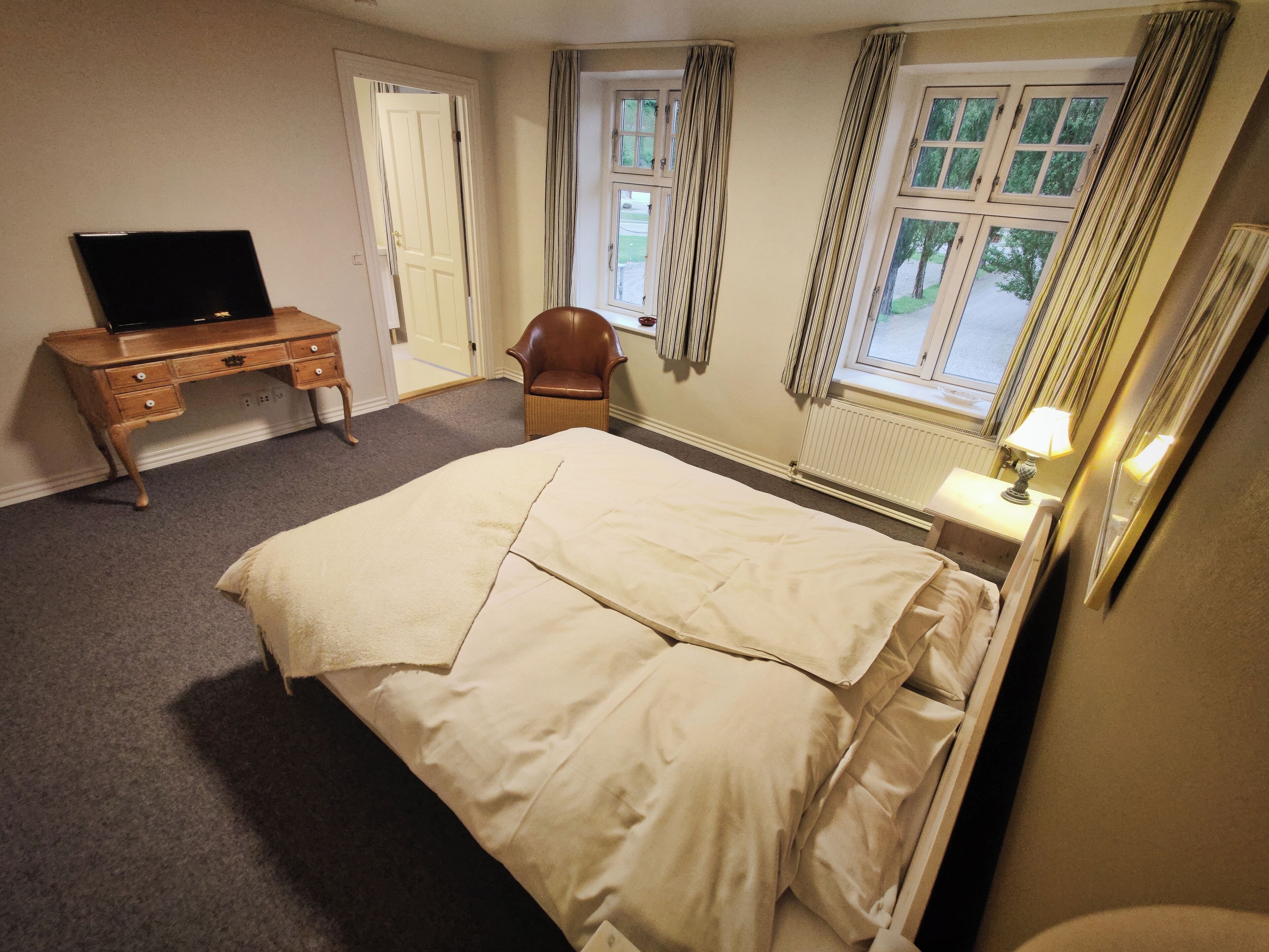 Un dormitorio con cama, escritorio, silla, ventana con cortinas y lámpara.