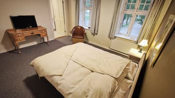 Un dormitorio con cama, escritorio, silla, ventana con cortinas y lámpara.