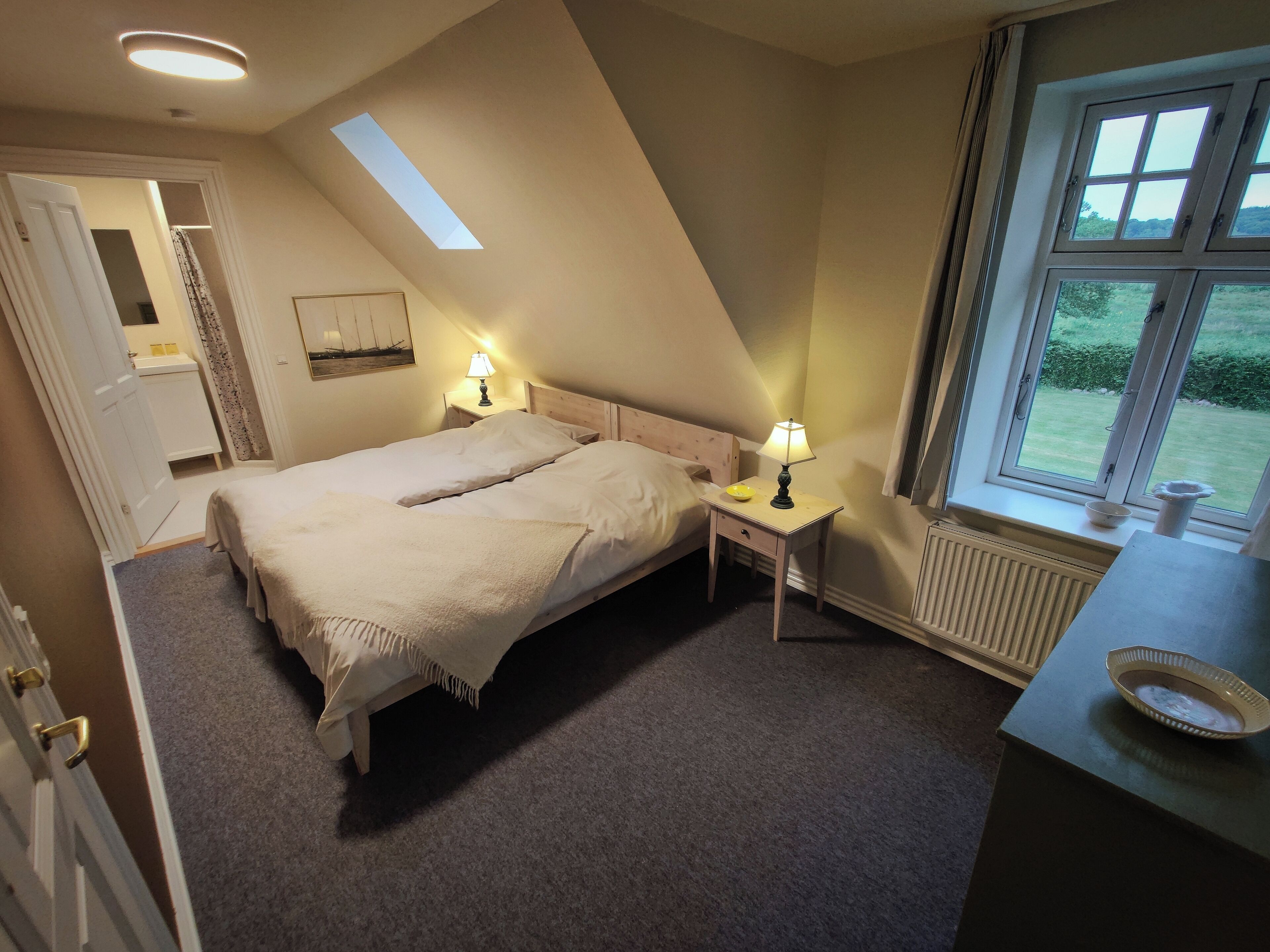Un dormitorio con una cama grande, una mesita de noche con lámpara, una ventana con vistas al exterior y un radiador.