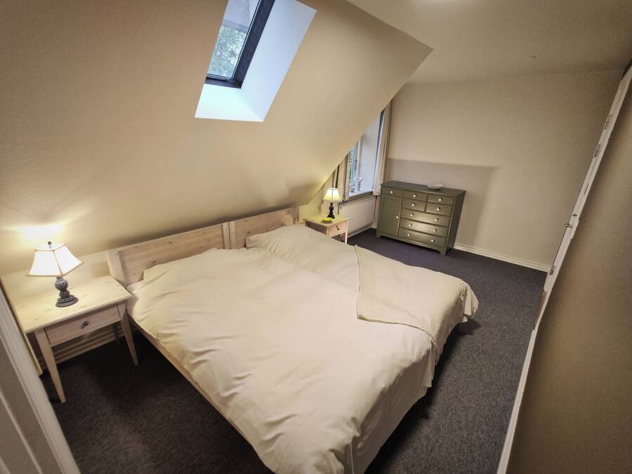 A bedroom with a single bed, a nightstand, a dresser, and a small window.