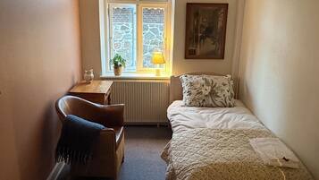 A small, cozy room with a single bed, a chair, a desk, and a window with a view.