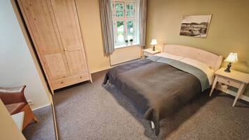 A bedroom with a bed, a wooden wardrobe, a nightstand with a lamp, and a window with curtains.