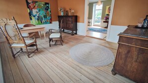 A room with wooden flooring, a dining table, two chairs, a large rug, a wooden cabinet, and a painting on the wall. - Aamølle Gæstgiveri (Hadsund)