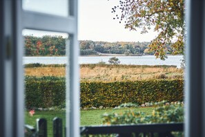 A view through a window of a lake with a forested hill in the background. - Aamølle Gæstgiveri (Hadsund)
