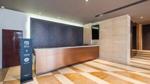 A modern reception area with a dark textured wall, a reception desk, and a check-in counter. - Le Peng hotel (Tianjin)