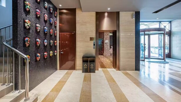 A modern lobby with a marble floor, a wall of colorful masks, a trash bin, and a glass door leading to another area. - Le Peng hotel (Tianjin)