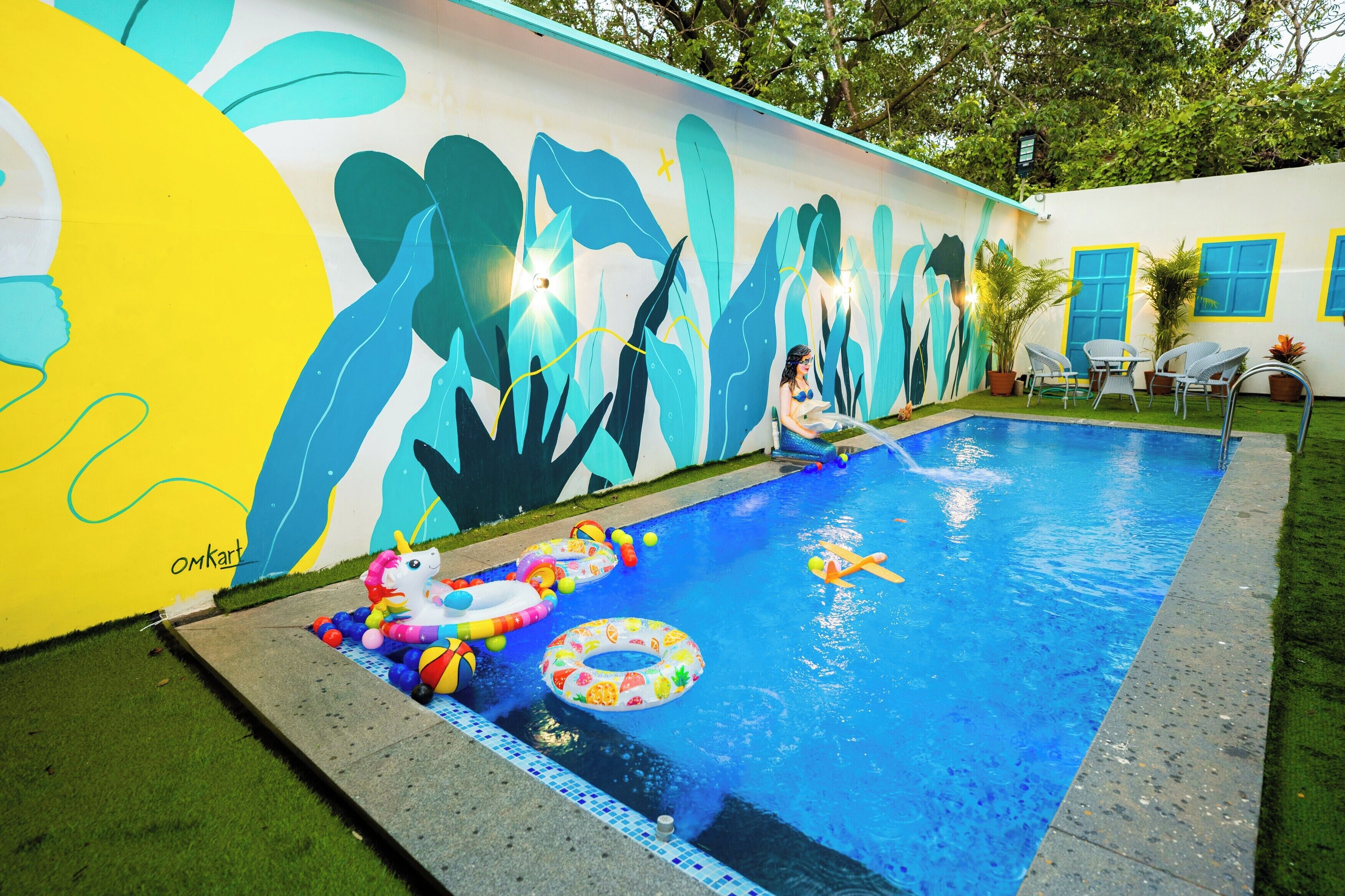 Una piscina con un mural, aros inflables y un pequeño unicornio inflable.