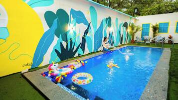 Una piscina con un mural, aros inflables y un pequeño unicornio inflable.