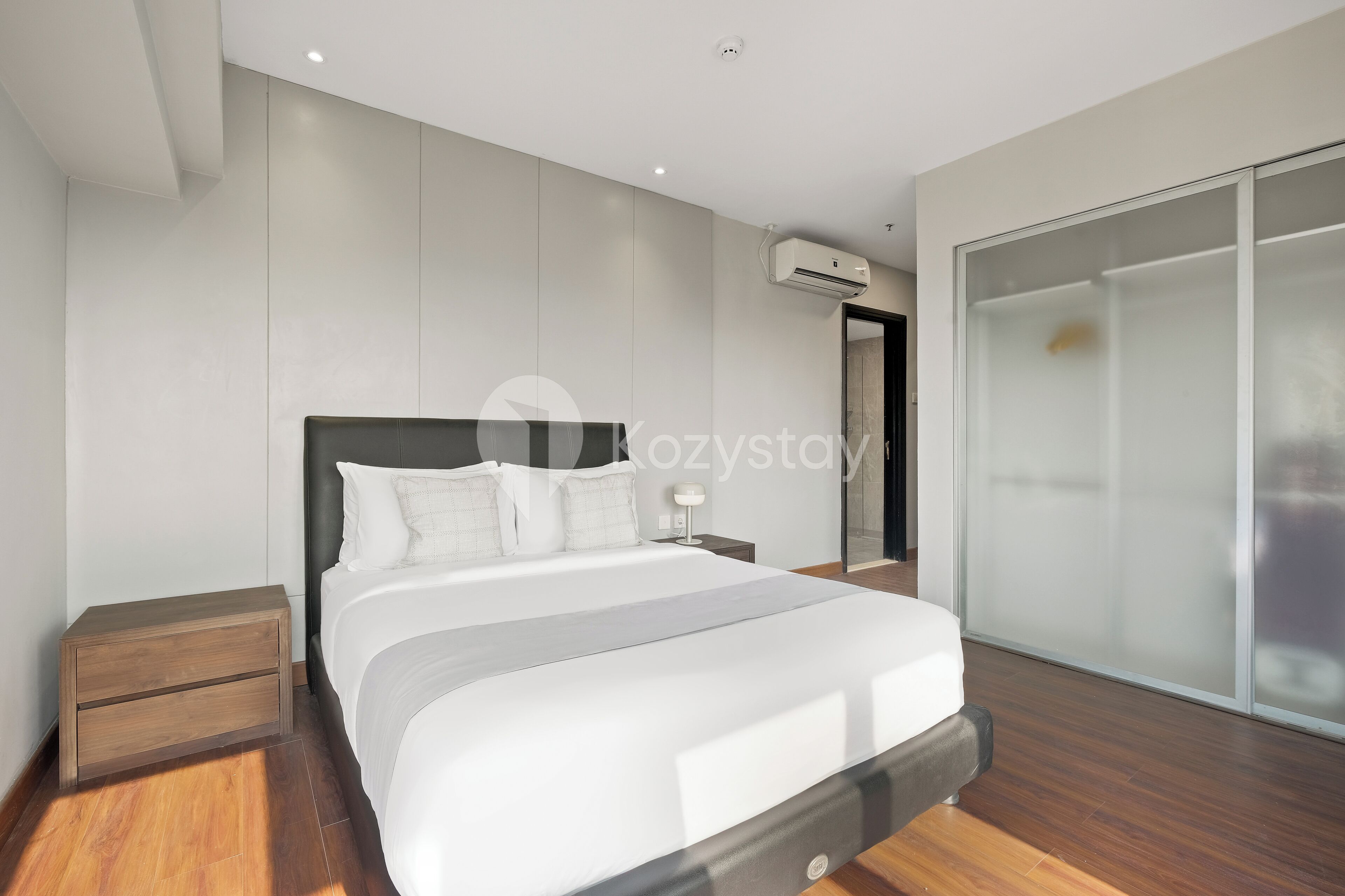 A modern bedroom with a large bed, a nightstand, a bedside table, and a large window with frosted glass.