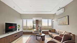 Een moderne woonkamer met een flatscreen-tv, een bank, een salontafel en een groot raam met uitzicht op de omgeving.