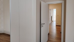 Un couloir au plancher en bois mène à une pièce dont la porte est blanche.