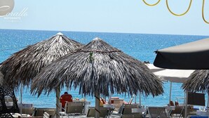 Un restaurant situé en bord de mer, doté de parasols en chaume et de chaises longues.