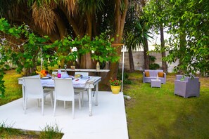 An outdoor patio with a table and chairs, surrounded by greenery and a stone wall.