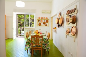 A dining area with a table set for four, a window with a view of greenery, and a wall with copper pots and pans. - Dimora San Pancrazio (San Pancrazio Salentino)