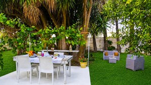 Un patio al aire libre con una mesa y sillas, rodeado de follaje y un muro de piedra.