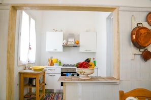 A kitchen with white cabinets, a gas stove, a wooden table with a yellow bowl, and a fruit bowl on the counter.