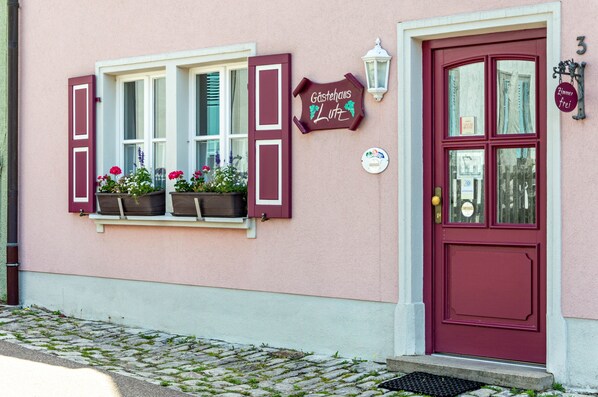 Un bâtiment avec une porte rouge, une fenêtre avec des volets et une enseigne sur laquelle on peut lire « Gästehaus Lutz ».