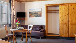 A room with a wooden table, two chairs, a sofa, a TV, a painting, and a wardrobe. - Room 'Lutz - Zimmer 1' with Shared Terrace, Shared Garden and Wi-Fi (Iphofen)