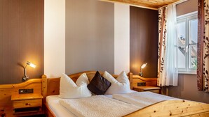 A wooden bed with a white bedspread and pillows, two bedside tables with lamps, and a window with curtains. - Room 'Lutz - Zimmer 1' with Shared Terrace, Shared Garden and Wi-Fi (Iphofen)