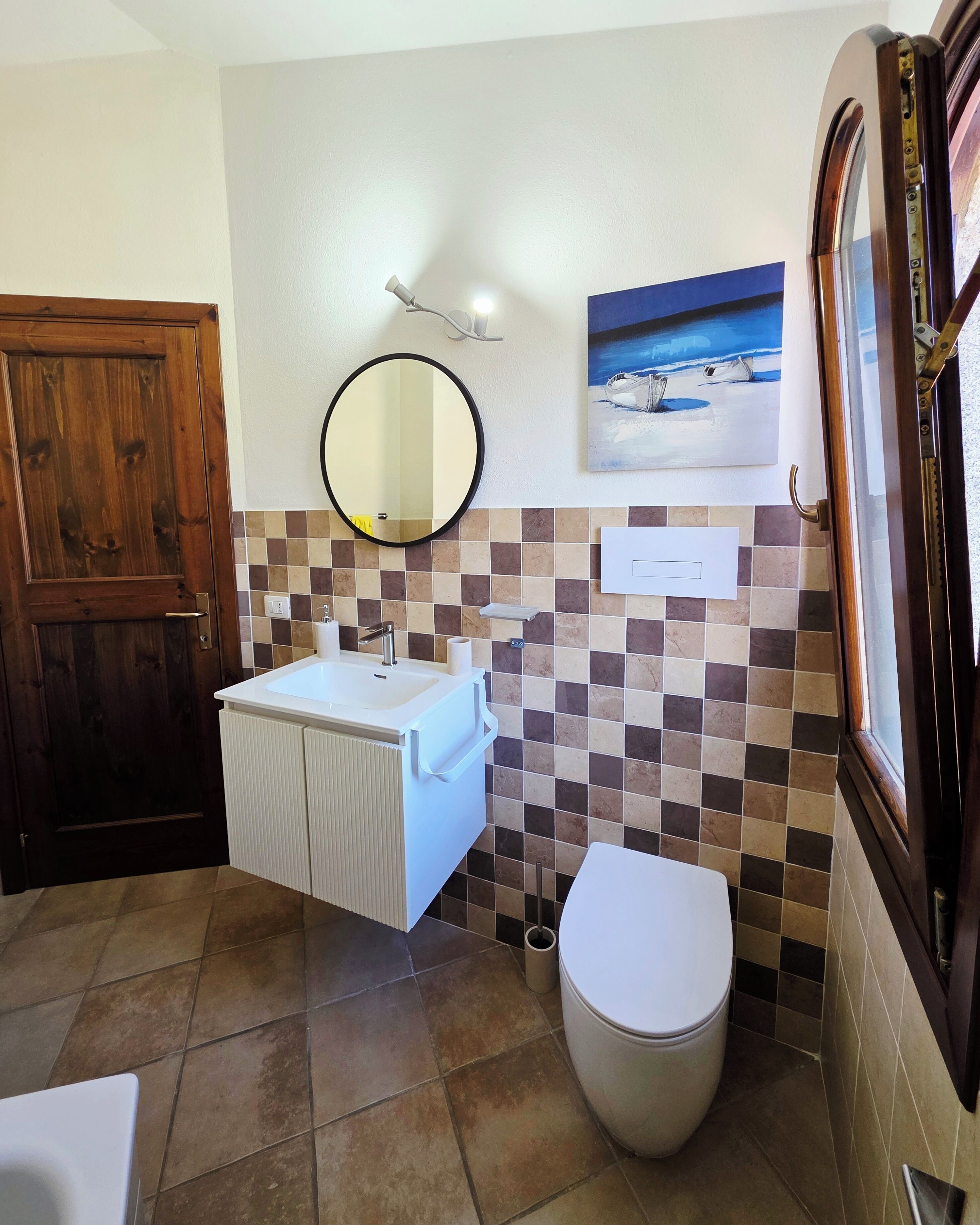 Un baño con puerta de madera, un lavamanos blanco con espejo, un inodoro y un salpicadero de azulejos.