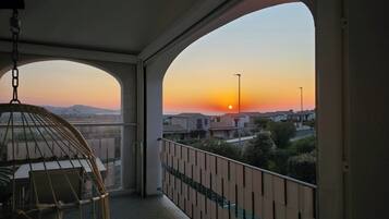 A balcony with a view of the sunset, a hanging chair, and a railing.