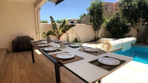 Une table à manger installée à l’extérieur, avec une piscine en arrière-plan.
