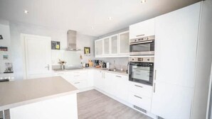 Une cuisine moderne avec des meubles blancs, des appareils en acier inoxydable et un revêtement de sol de couleur claire.