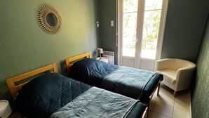 A room with two wooden beds, a small white chair, a wall-mounted mirror, and a window with a view of greenery. - Group gîte, many activities, river, footbridge, dogs ok, nature (Mazamet)