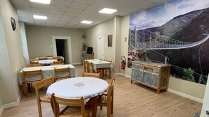 A dining area with round tables and chairs, a mural of a bridge, and a fire extinguisher on the wall. - Group gîte, many activities, river, footbridge, dogs ok, nature (Mazamet)