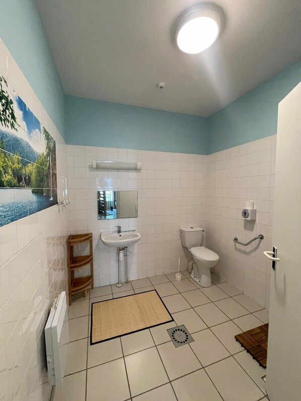 A bathroom with white tiles, a sink, a toilet, a mirror, and a shower area.