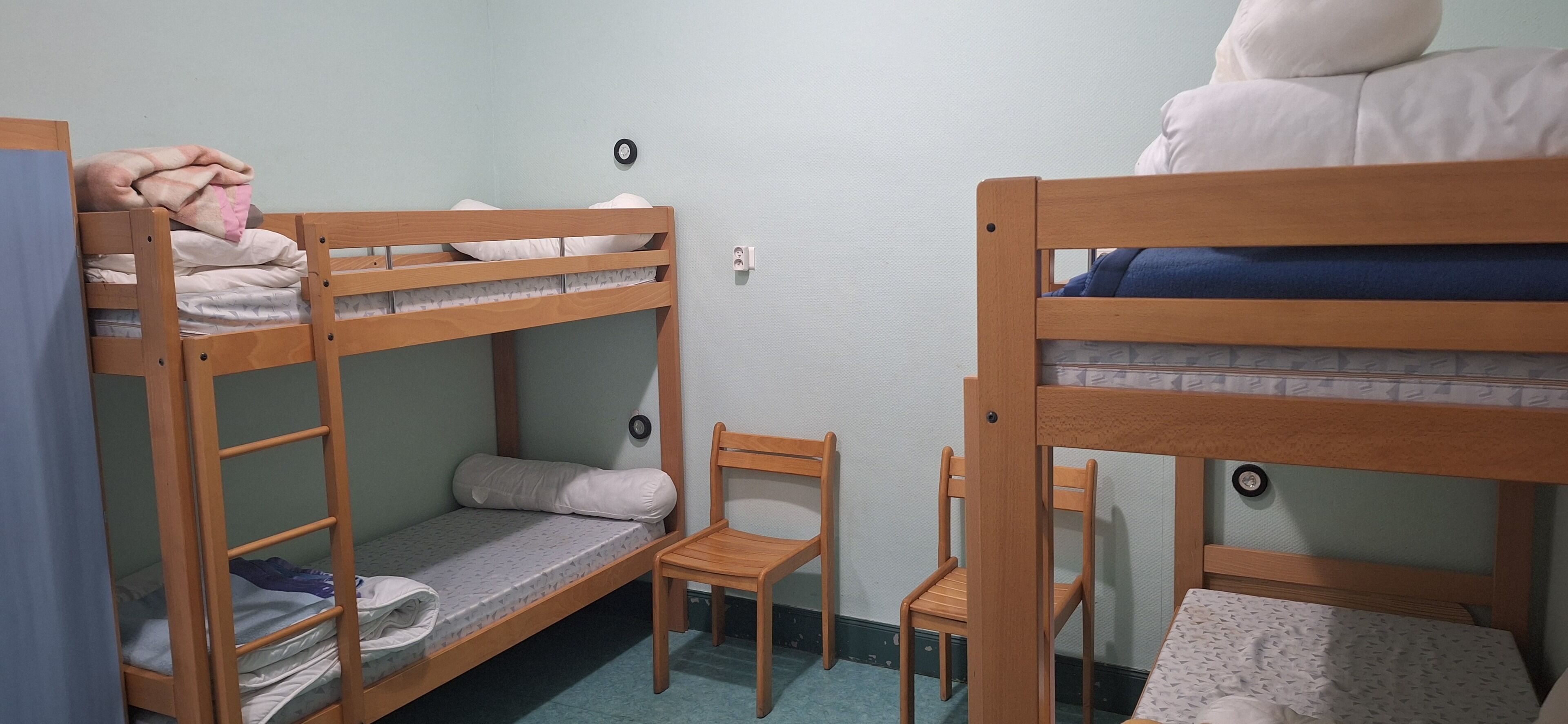 A dormitory room with bunk beds, a chair, and a small table.