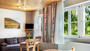 A room with a bed, a wooden table with chairs, a sofa, a TV, and a window with curtains. - Room 'Lutz - Zimmer 2' with Shared Terrace, Shared Garden and Wi-Fi (Iphofen)