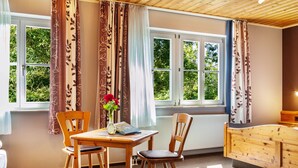 A room with a wooden table, two chairs, a vase with flowers, and a window with curtains. - Room 'Lutz - Zimmer 2' with Shared Terrace, Shared Garden and Wi-Fi (Iphofen)