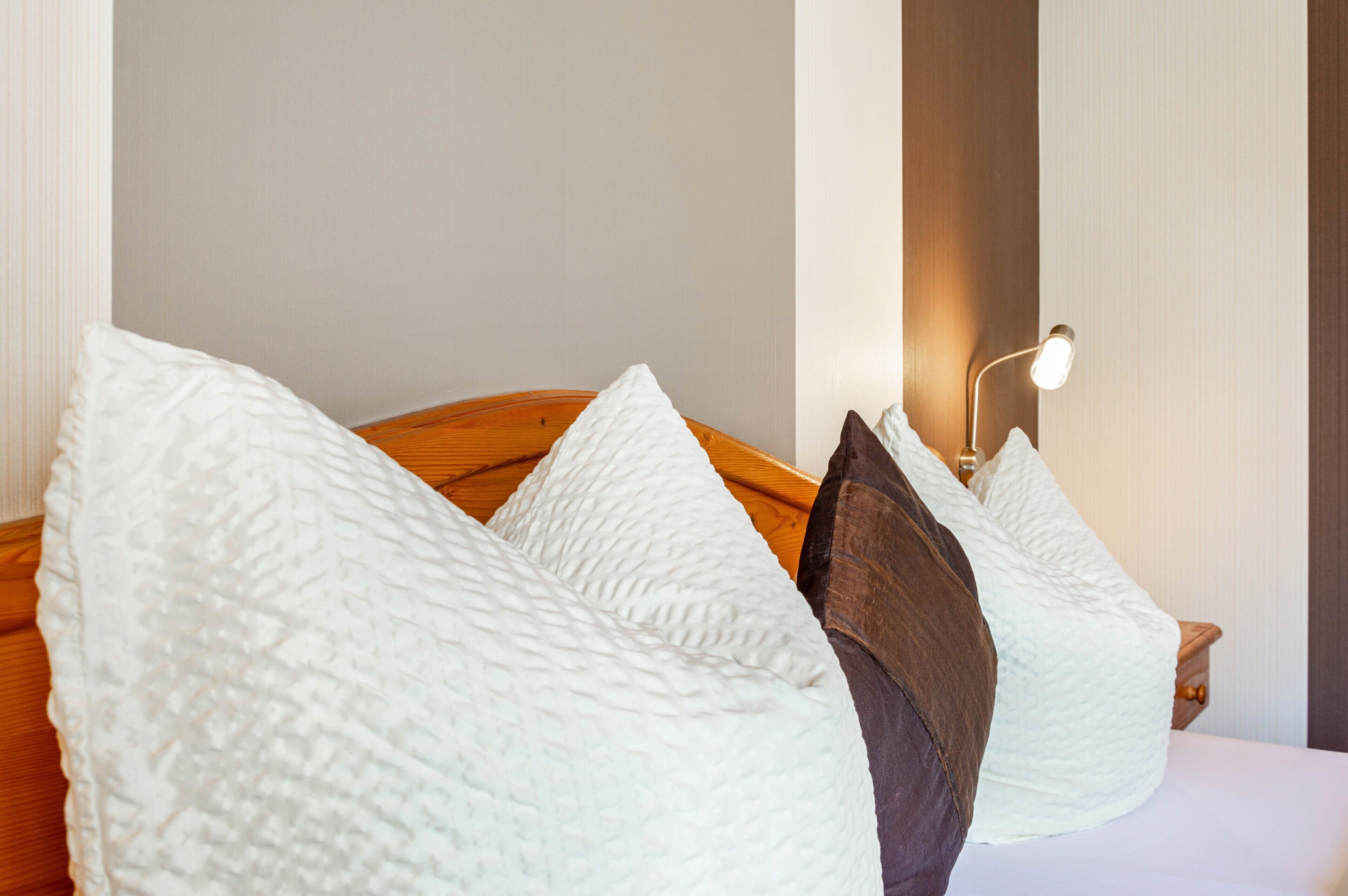Una cama con almohadas blancas y marrones, un cabecero de madera y una lámpara de noche.