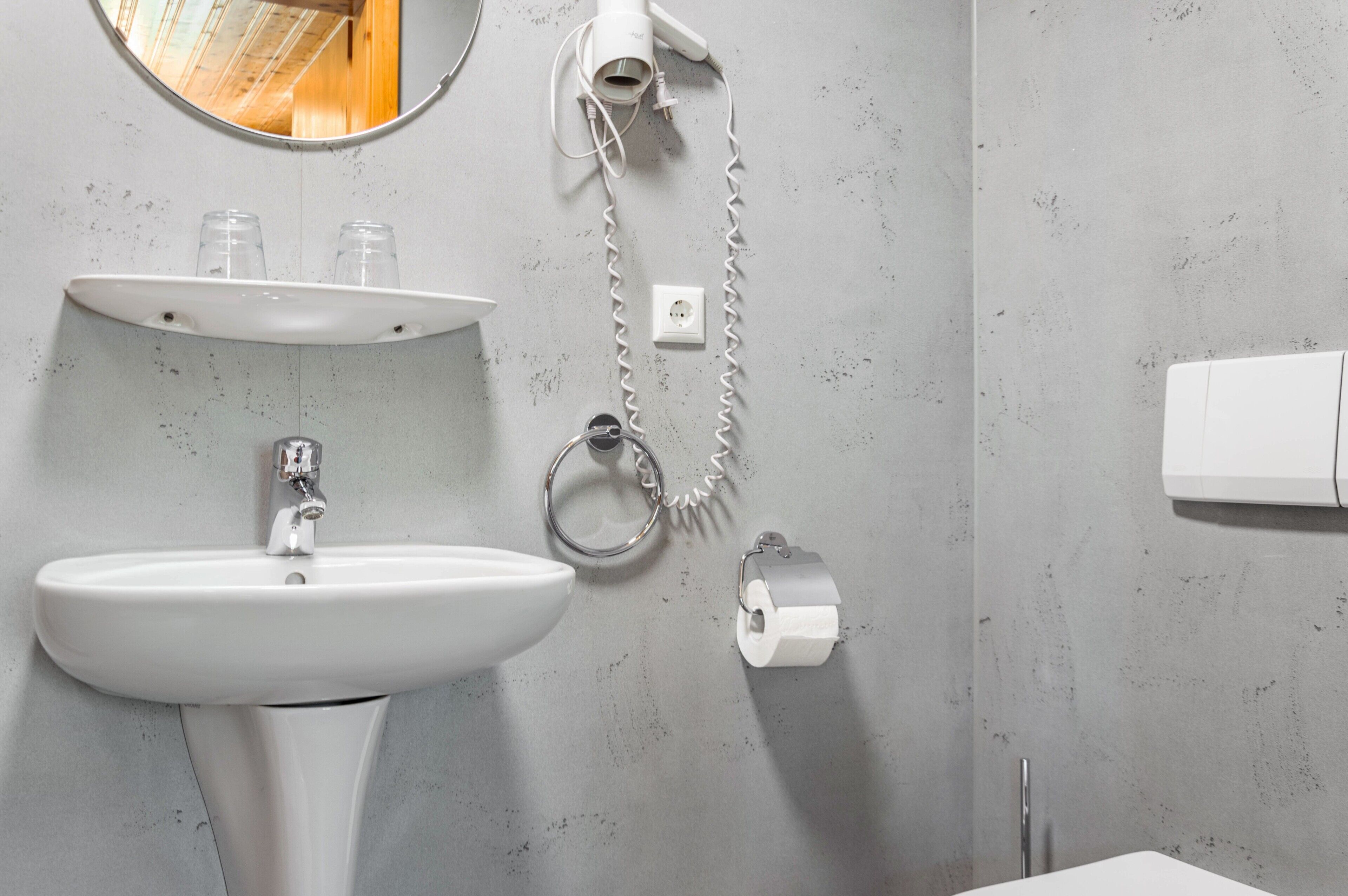 A bathroom with a white sink, a mirror, a hairdryer, and a toilet paper holder.
