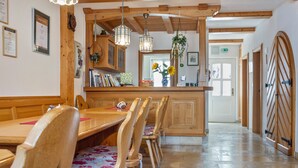 A wooden dining area with a long table and chairs, a kitchen area with hanging lights, and a door with a unique design. - Room 'Lutz - Zimmer 3' with Shared Terrace, Shared Garden and Wi-Fi (Iphofen)