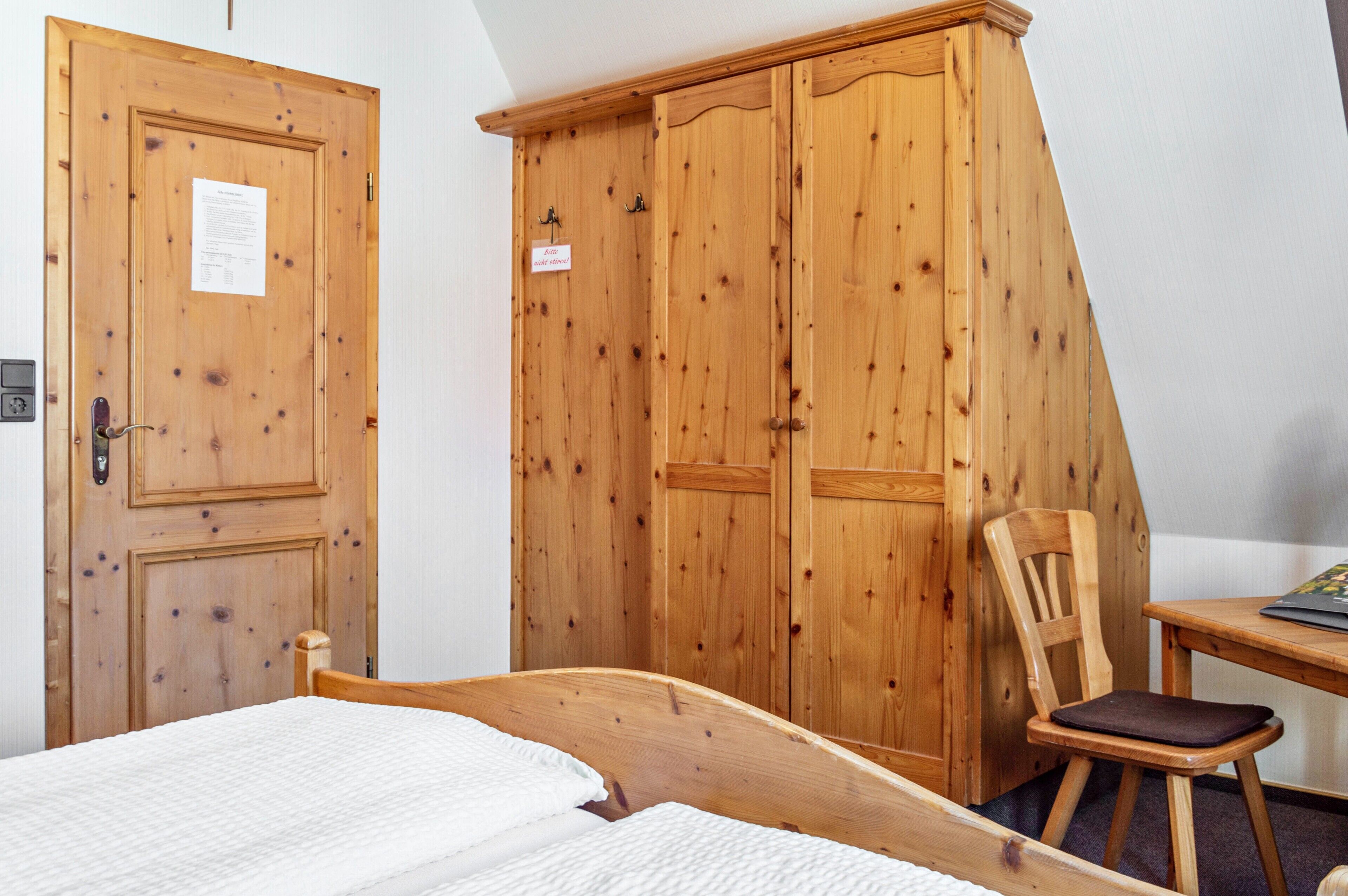 Un dormitorio con un armario de madera, una cama individual, una silla de madera y una mesita.