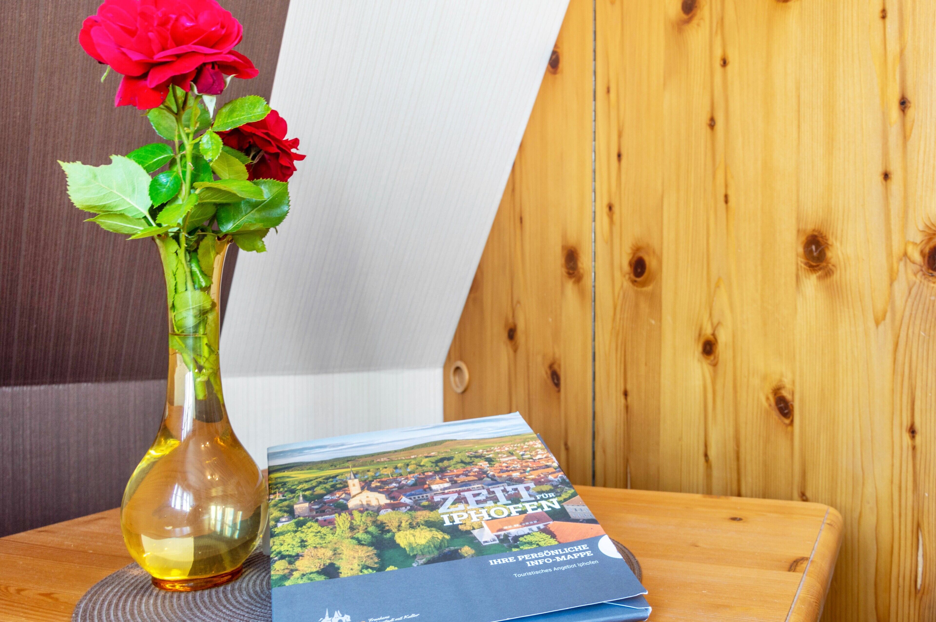 A wooden table with a vase containing red roses and a brochure titled 'ZEIT FÜR IPHOFEN'.