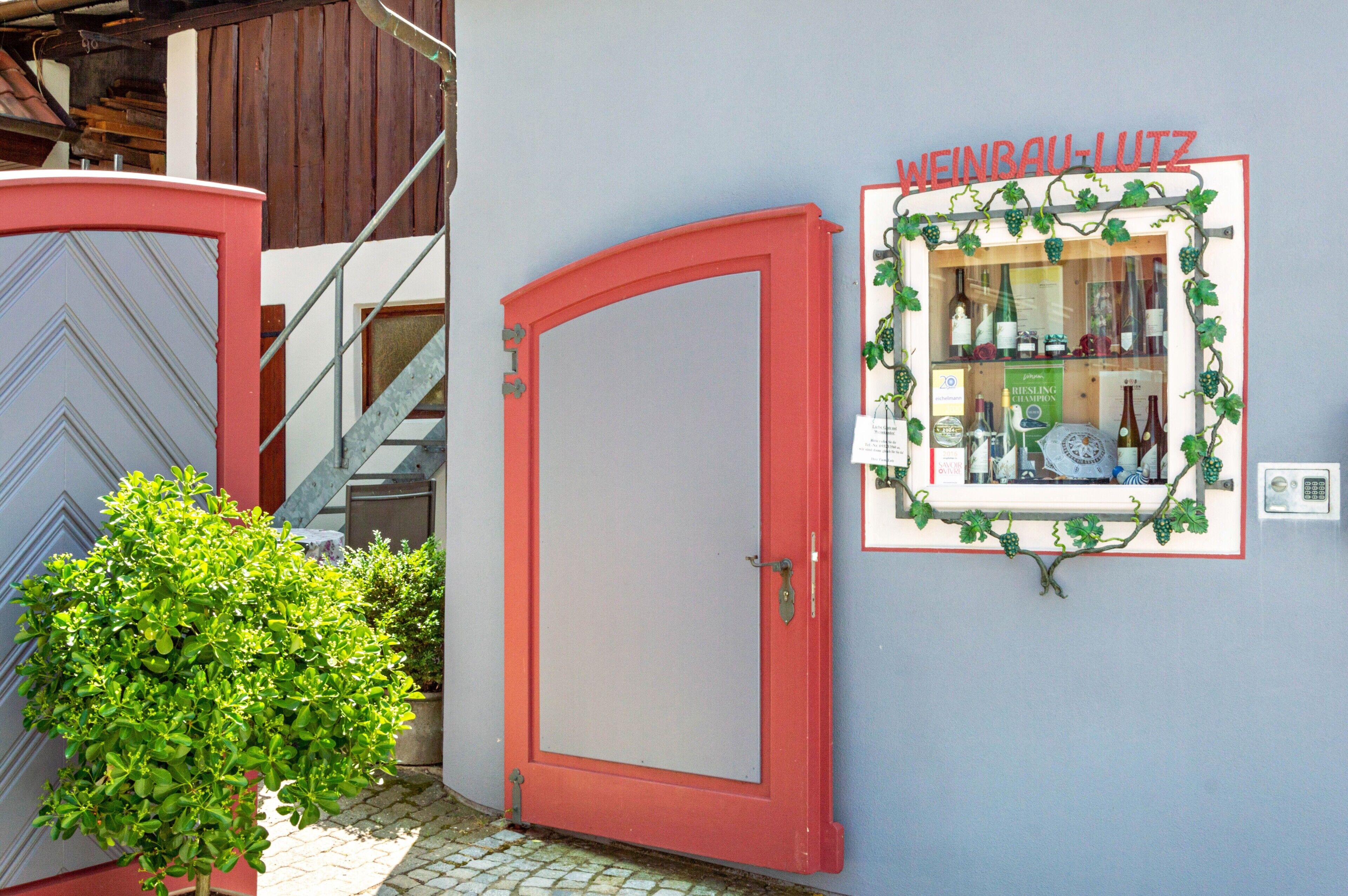 A red door, a small potted plant, and a framed wine display on a wall.