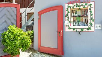 A red door, a small potted plant, and a framed wine display on a wall.