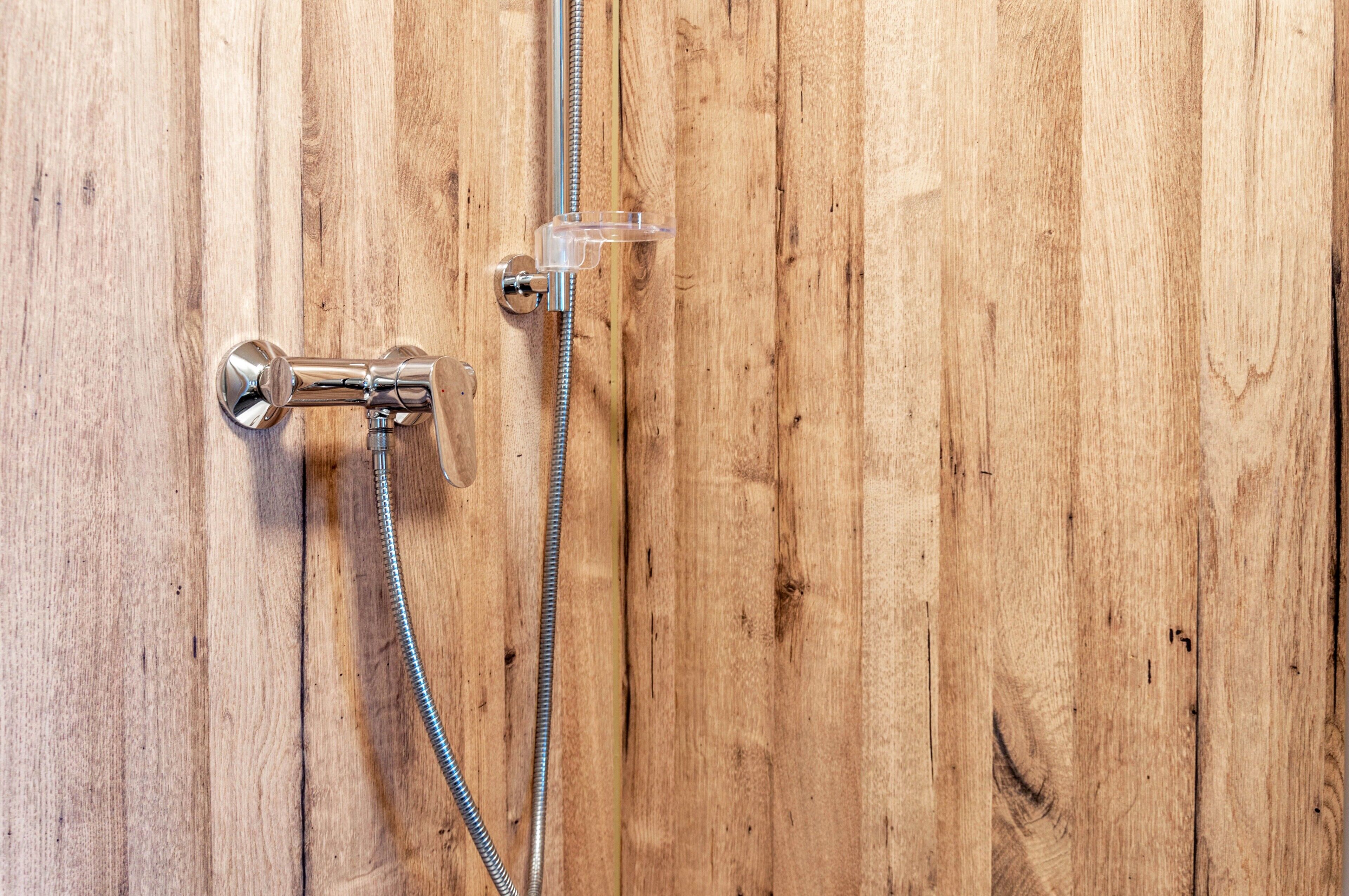 A shower with a chrome faucet and hose against a wooden wall.