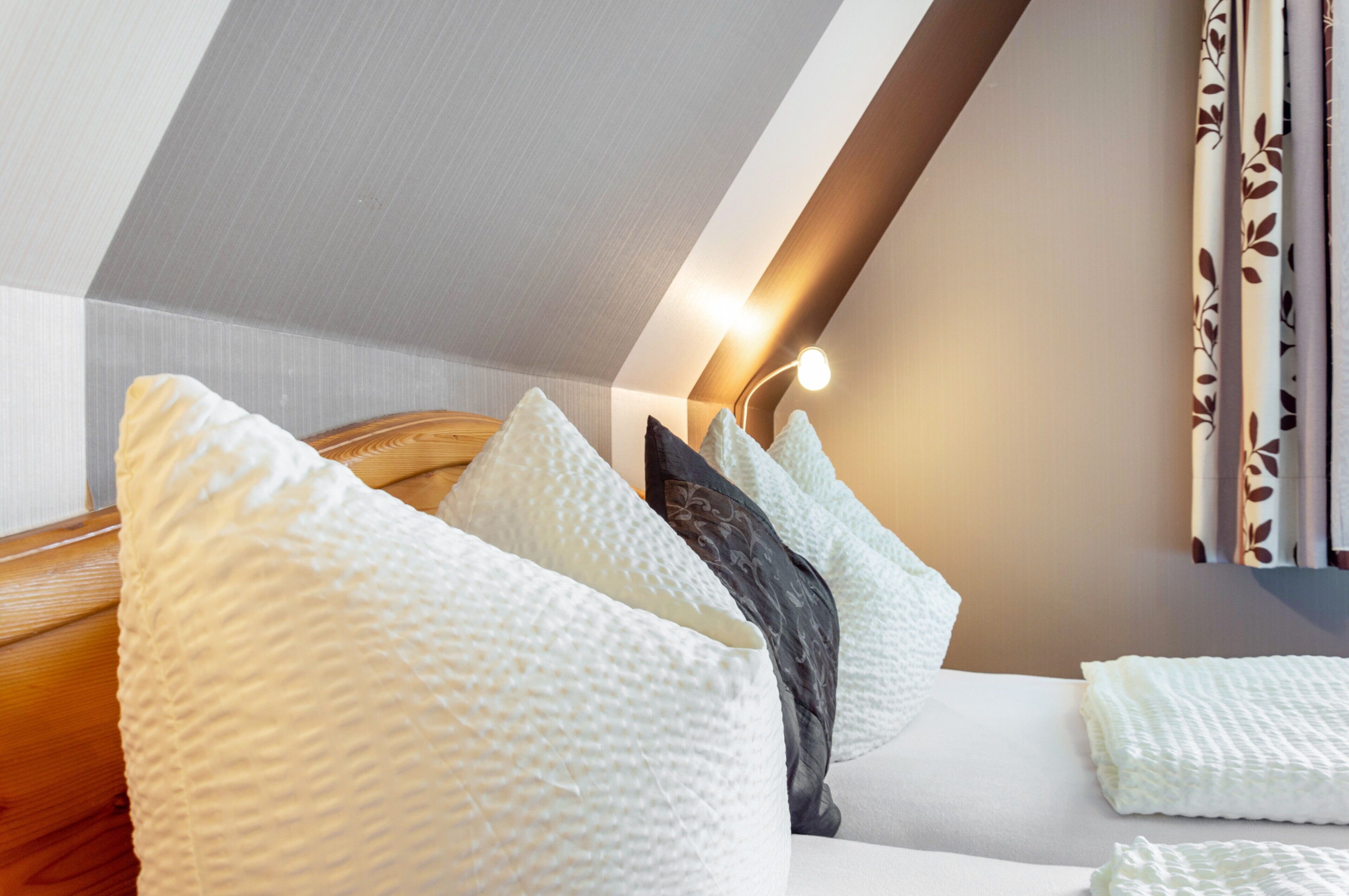 Ein Schlafzimmer mit schrägem Dach, einem Bett mit weißer Bettwäsche und einer Wandleuchte.