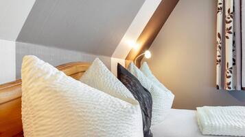 Ein Schlafzimmer mit schrägem Dach, einem Bett mit weißer Bettwäsche und einer Wandleuchte.
