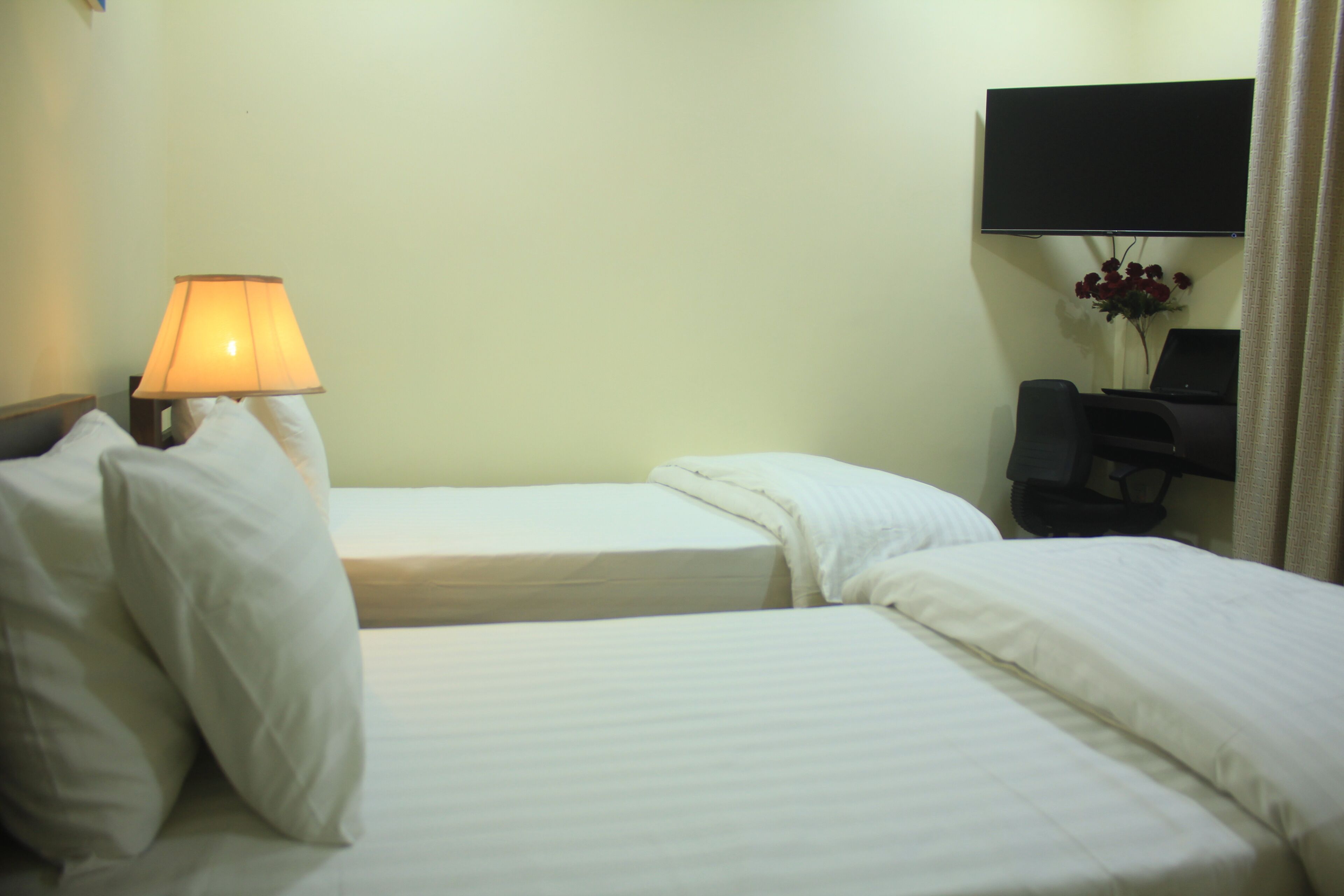 Habitación de hotel con dos camas, una lámpara de noche, un televisor de pantalla plana montado en la pared y un escritorio con una silla.