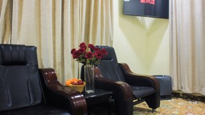 A room with two leather chairs, a vase with flowers, a fruit basket, and a television displaying 'NETFLIX'.
