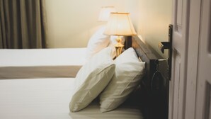 A hotel room with a bed, pillows, a bedside lamp, and a door.