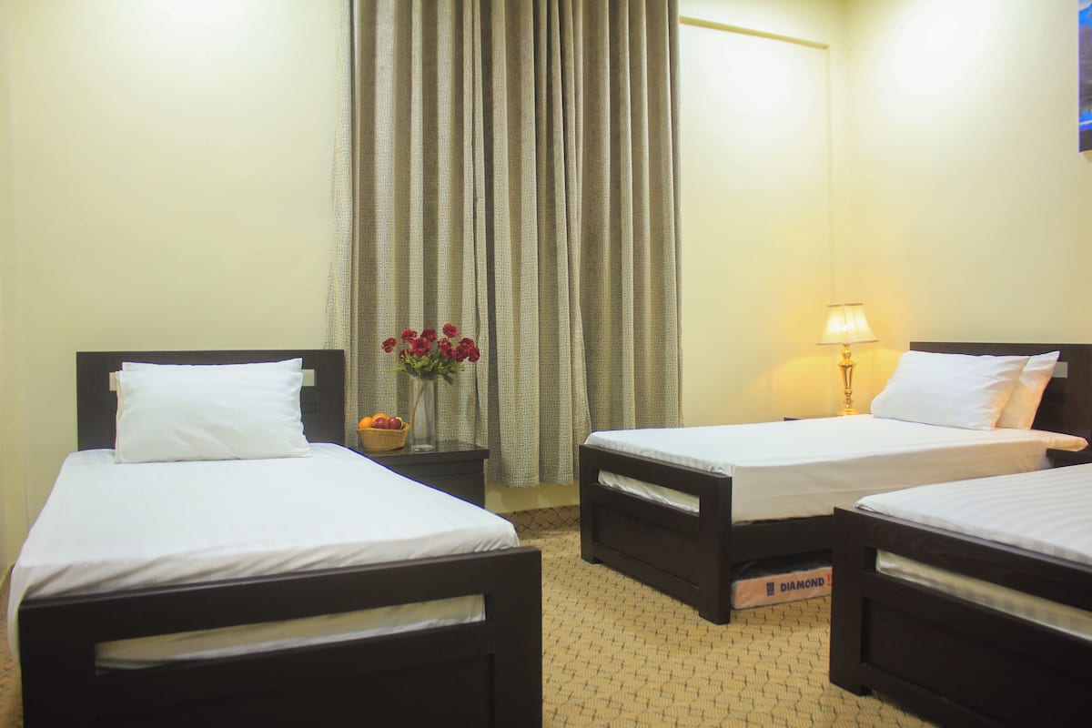 Une chambre d’hôtel avec deux lits simples, une table de chevet avec une lampe, un vase avec des fleurs et une fenêtre avec des rideaux.